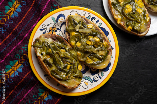 Molletes with poblano rajas and cheese on dark background. Mexican food
