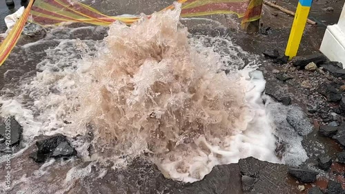 Close up slow-motion of water gushing out of a burst pipe in a damaged city road.