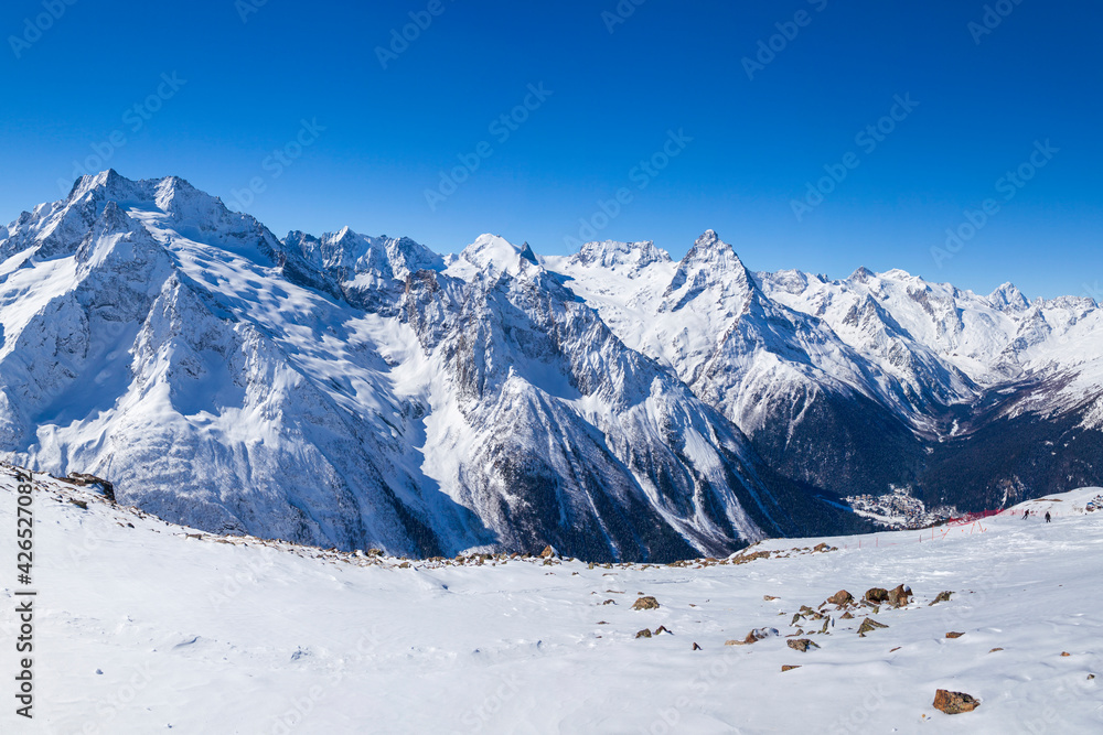 Caucasus Mountains, Panoramic view of the ski slope with the mountains Belalakaya, Sofrudzhu and Sulakhat on the horizon in winter day. Dombai ski resort, Western Caucasus