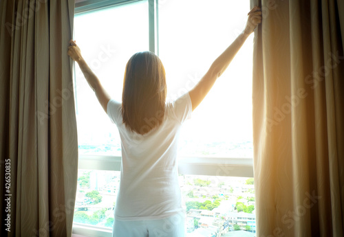 Morning of a new day, Women wake up from bed. In the morning, she opens the curtains in her bedroom for fresh air and natural morning sunshine.