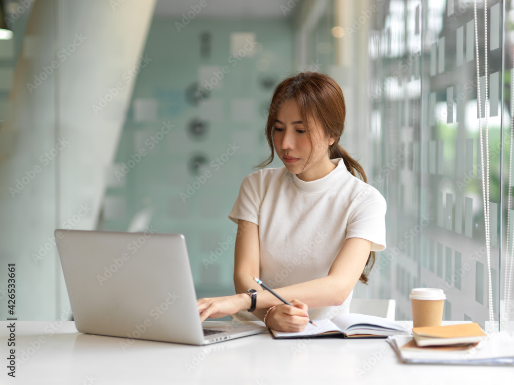 Female student doing assignment with laptop and paperwork in office room Female student doing assignment with laptop and paperwork in office room