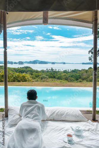 Happy man traveler enjoy Beautiful ocean view, Tourist relaxing in tropical luxury resort with swimming pool. Leisure, travel and summer vacation concept