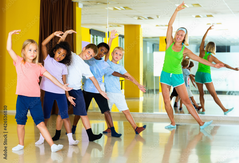 Happy cheerful smiling preteen dancers practicing dance routine with female choreographer in modern studio.