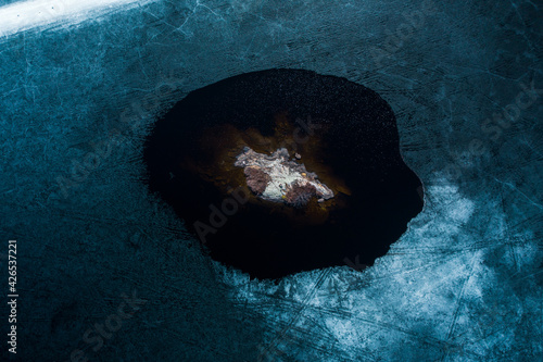 Bright blue ice slowly melting at shoreline as warm sunshine heats up a rock island.  Spring time in Northern Canadian Shield.