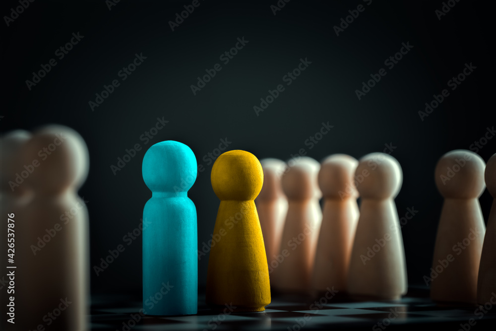 Blue wooden dolls for men and yellow for women. Representatives of the two teams are facing each other on a chessboard. Business competition. Two colleagues having disagreement and conflict. Blue wooden dolls for men and yellow for women. Representatives of the two teams are facing each other on a chessboard. Business competition. Two colleagues having disagreement and conflict.