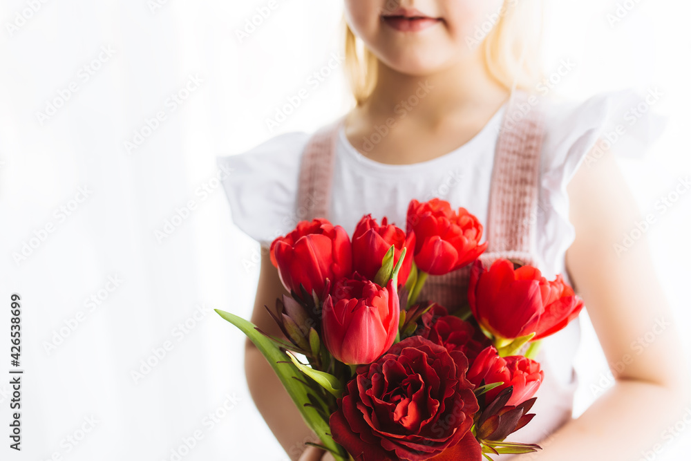 Smiling small girl holding bouquet of red tulips. Concept for greeting card
