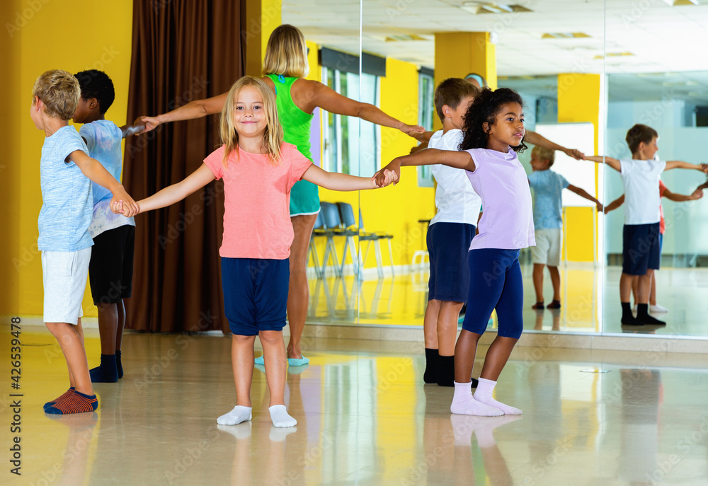 Group of glad cheerful positive tweens exercising folk dance, forming circle with female coach in choreography class