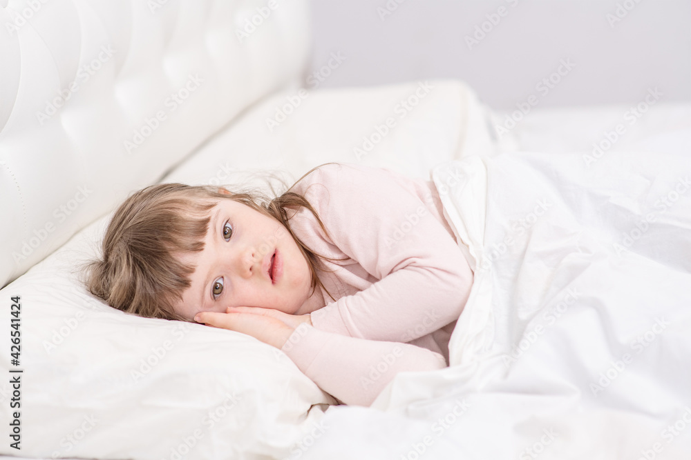 A girl with down syndrome lying on the bed under the covers and getting ready for bed. Usually childhood in a family for children with disabilities A girl with down syndrome lying on the bed under the covers and getting ready for bed. Usually childhood in a family for children with disabilities