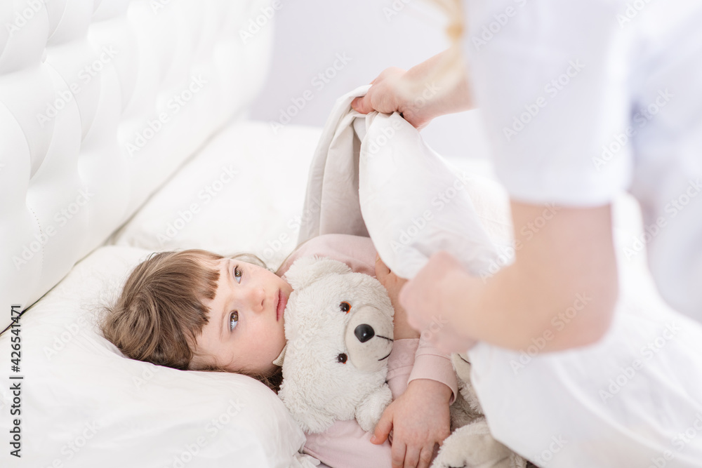 Mom covering a girl with down syndrome with a blanket. Ordinary childcare in a family for children with disabilities Mom covering a girl with down syndrome with a blanket. Ordinary childcare in a family for children with disabilities