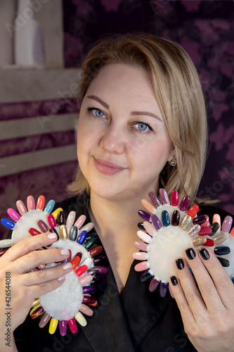 Portrait of a woman with varnish palettes. Close-up portrait of a manicure master in the workplace with palettes of multi-colored varnish. Manicurist in a black jacket at the workplace. 