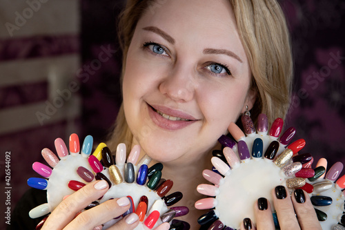 Portrait of a woman with varnish palettes. Close-up portrait of a manicure master in the workplace with palettes of multi-colored varnish. Manicurist in a black jacket at the workplace. 