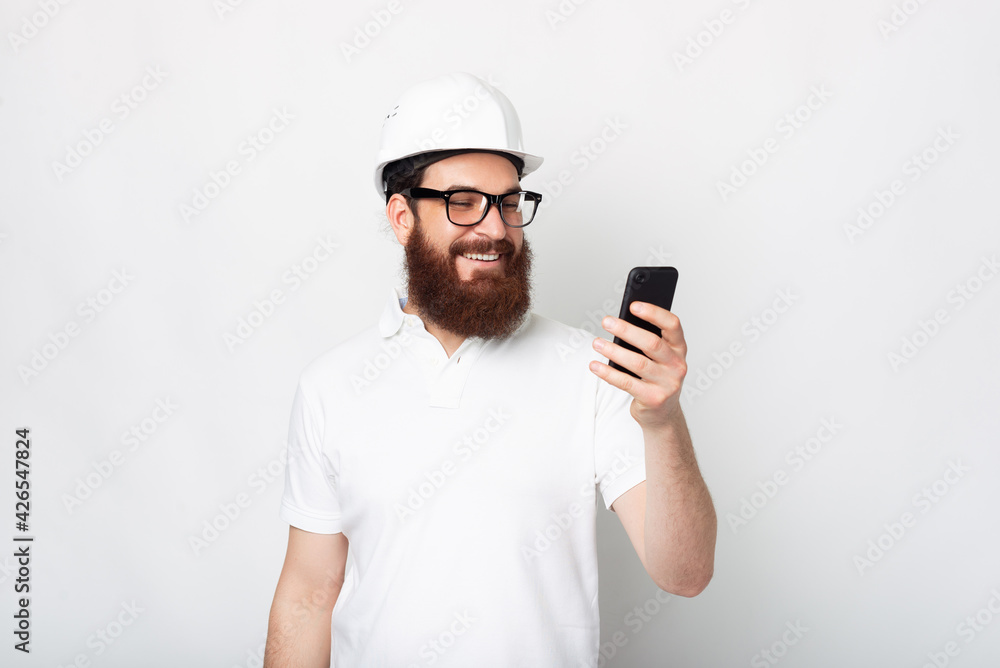 Photo of cheerful engineer man using smartphone and wearing hard hat Photo of cheerful engineer man using smartphone and wearing hard hat