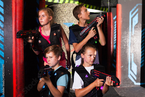 Group portrait of happy teenagers with laser guns having fun on dark lasertag arena..