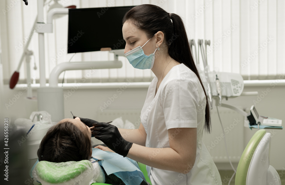 A woman dentist in gloves and a medical mask operates on a patient using equipment - a microscope. The office of the modern dentist. A woman dentist in gloves and a medical mask operates on a patient using equipment - a microscope. The office of the modern dentist.