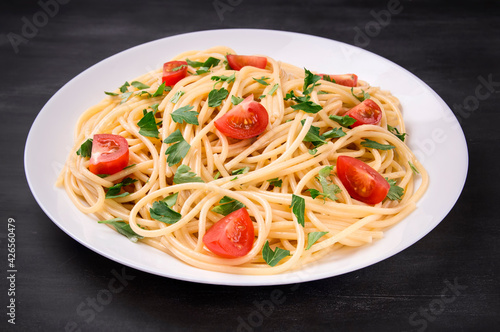 Pasta spaghetti with cherry tomatoes and parsley on a dark background