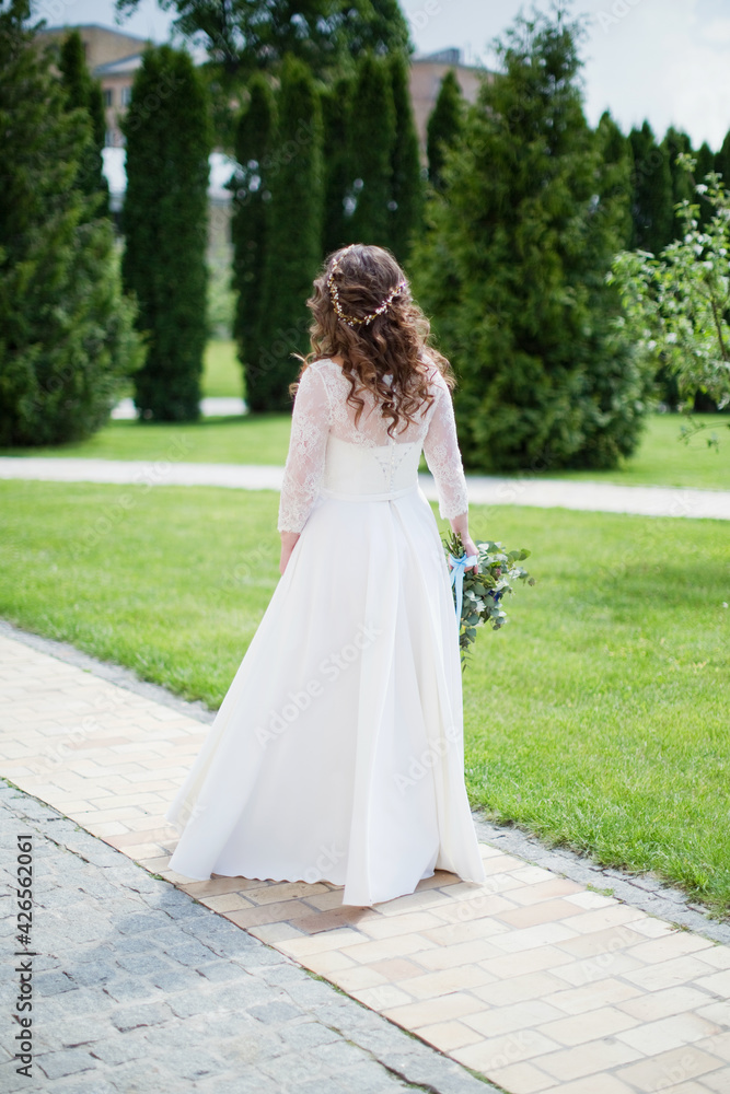 Bride in a white wedding dress stands in the park