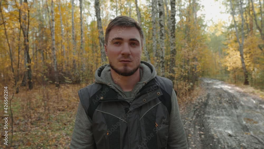 A Suspicious Young Man Walks On A Dirt Road In The Middle Of An Autumn Yellow Forest And Looks To The Sides. Serious Facial Expression. Lost Man in the Forest, Forester, Hunter, Lumberjack A Suspicious Young Man Walks On A Dirt Road In The Middle Of An Autumn Yellow Forest And Looks To The Sides. Serious Facial Expression. Lost Man in the Forest, Forester, Hunter, Lumberjack