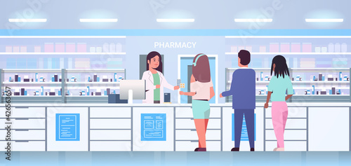 female doctor pharmacist giving pills to mix race customers patients at pharmacy counter modern drugstore interior medicine healthcare concept horizontal full length