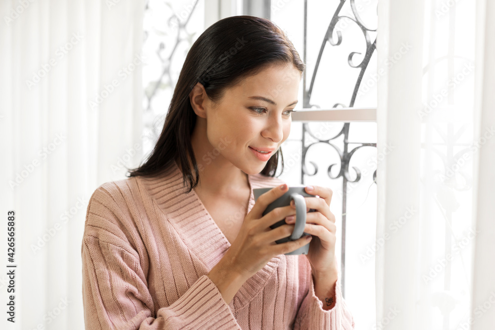 Portrait of smiling happy cheerful beautiful pretty caucasian woman relaxing drinking and looking at cup of hot coffee or tea.Girl felling enjoy having breakfast in holiday morning vacation at home Portrait of smiling happy cheerful beautiful pretty caucasian woman relaxing drinking and looking at cup of hot coffee or tea.Girl felling enjoy having breakfast in holiday morning vacation at home