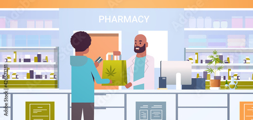 male doctor pharmacist giving medical cannabis package to african american client at pharmacy counter modern drugstore interior medicine healthcare concept horizontal portrait