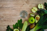 Glass with water and green vegetables and fruits on a wooden background.