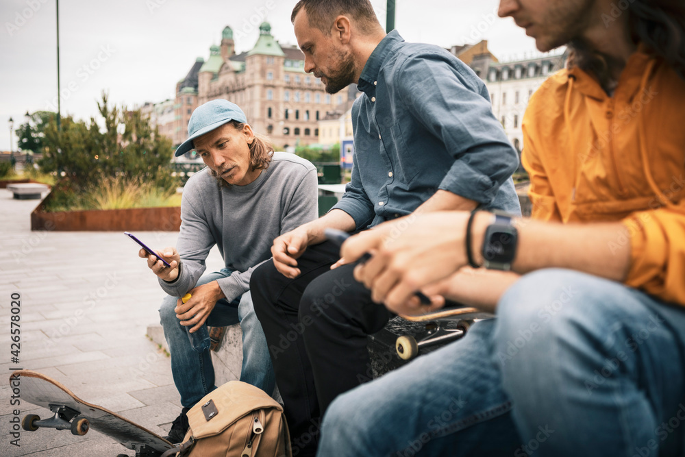 Male skaters using smart phone while sitting on footpath Male skaters using smart phone while sitting on footpath