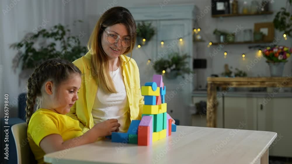 Happy family. Mom and daughter are building house from construction set. Family teamwork concept. Happy daughter builds house from colored constructor. Happy family with color constructor. Teamwork Happy family. Mom and daughter are building house from construction set. Family teamwork concept. Happy daughter builds house from colored constructor. Happy family with color constructor. Teamwork