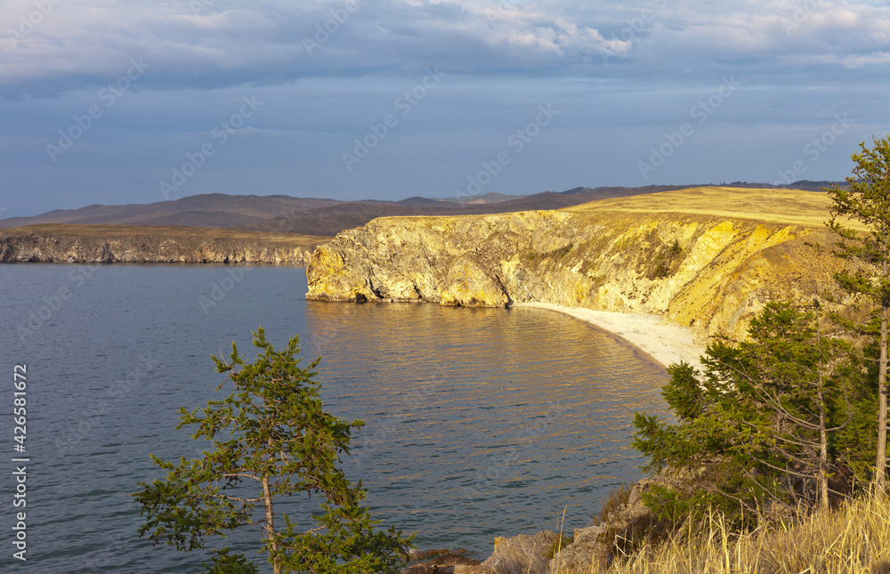 Baikal Lake at summer sunset. Beautiful landscape with coastal cloffs of Olkhon Island in the sunlight. Natural background. Summer travel and outdoor recreation Baikal Lake at summer sunset. Beautiful landscape with coastal cloffs of Olkhon Island in the sunlight. Natural background. Summer travel and outdoor recreation