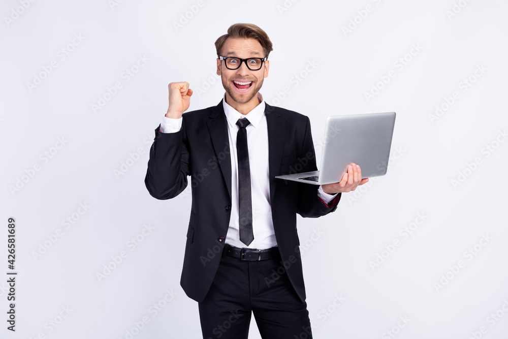 Photo of young man happy positive smile rejoice victory fists hand hold laptop isolated over grey color background Photo of young man happy positive smile rejoice victory fists hand hold laptop isolated over grey color background