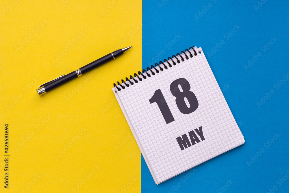 May 18th. Day 18 of month, calendar date. Notebook with a spiral and pen lies on a yellow-blue background May 18th. Day 18 of month, calendar date. Notebook with a spiral and pen lies on a yellow-blue background