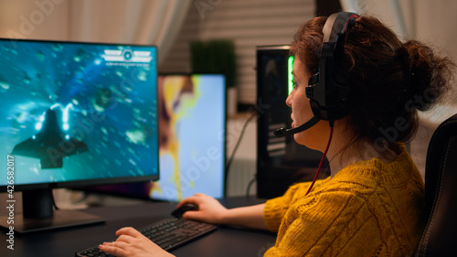 Professional esport woman gamer using mic of headset talking playing shooter game with team on streaming services. Virtual shooter game in cyberspace, esports player performing on pc gaming tournament