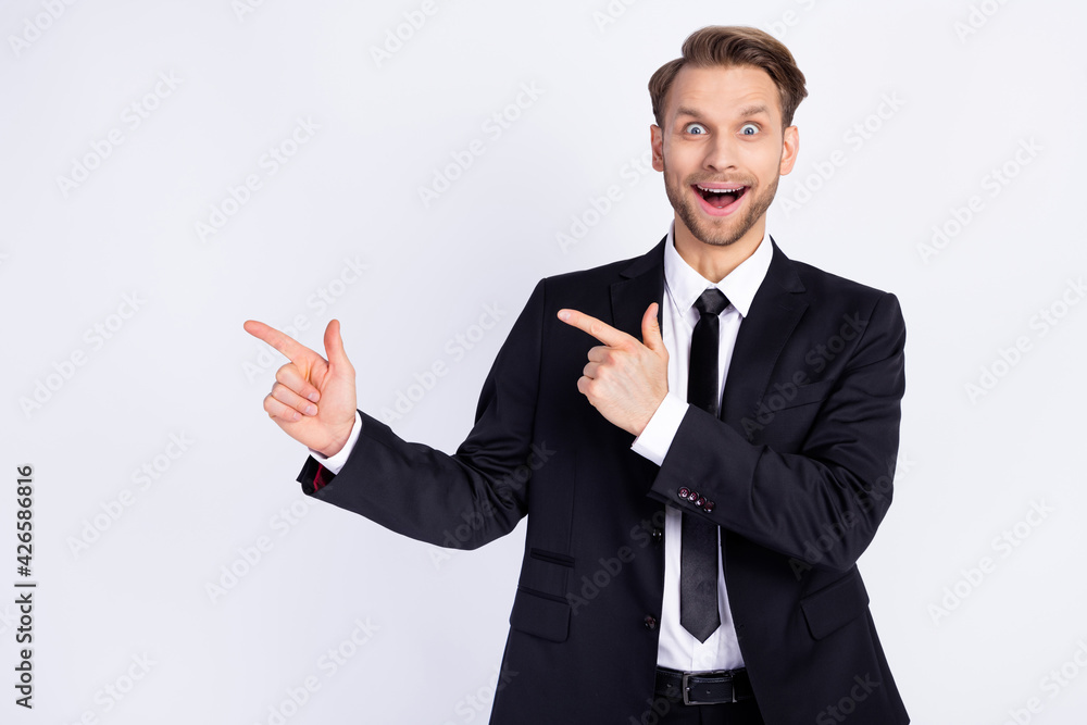 Photo of young excited man happy positive smile indicate fingers empty space ad advice choice isolated over grey color background Photo of young excited man happy positive smile indicate fingers empty space ad advice choice isolated over grey color background