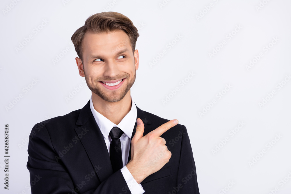 Photo of young man happy positive smile look indicate finger empty space ad advise choose isolated over grey color background Photo of young man happy positive smile look indicate finger empty space ad advise choose isolated over grey color background