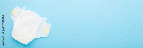 White soft new baby diaper on light blue table background. Pastel color. Closeup. Empty place for text or logo. Wide banner. Top down view.