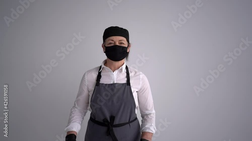 Portrait of a female cook in uniform and in a protective mask and gloves in black. A woman holding a wooden rolling pin. New reality. Cook or pastry chef, startup during a pandemic photo