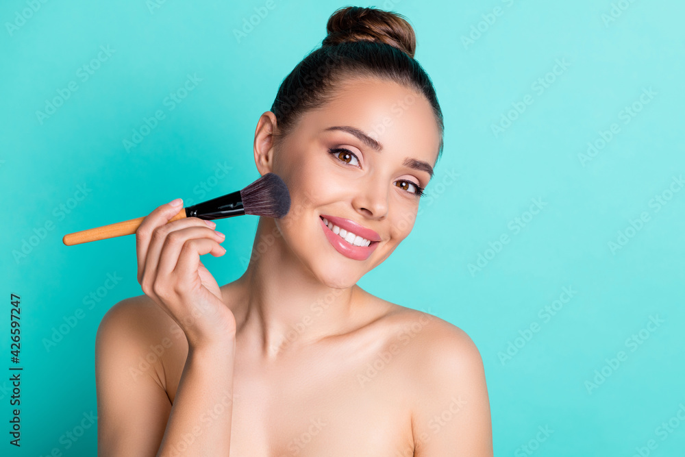 Portrait of attractive trendy cheerful girl using brush applying cc tone cream base isolated over bright teal turquoise color background Portrait of attractive trendy cheerful girl using brush applying cc tone cream base isolated over bright teal turquoise color background