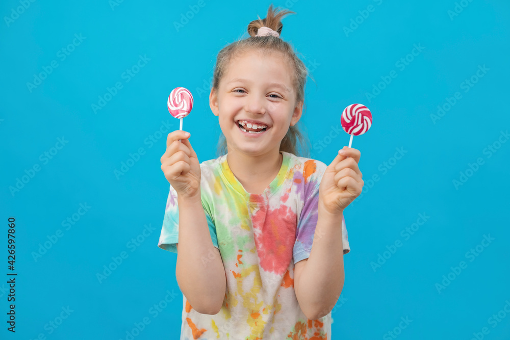 The concept of a holiday, fun entertainment and children's joy. A cute dark-haired girl in a multicolored T-shirt holds round lollipops and smiles. The concept of a holiday, fun entertainment and children's joy. A cute dark-haired girl in a multicolored T-shirt holds round lollipops and smiles.