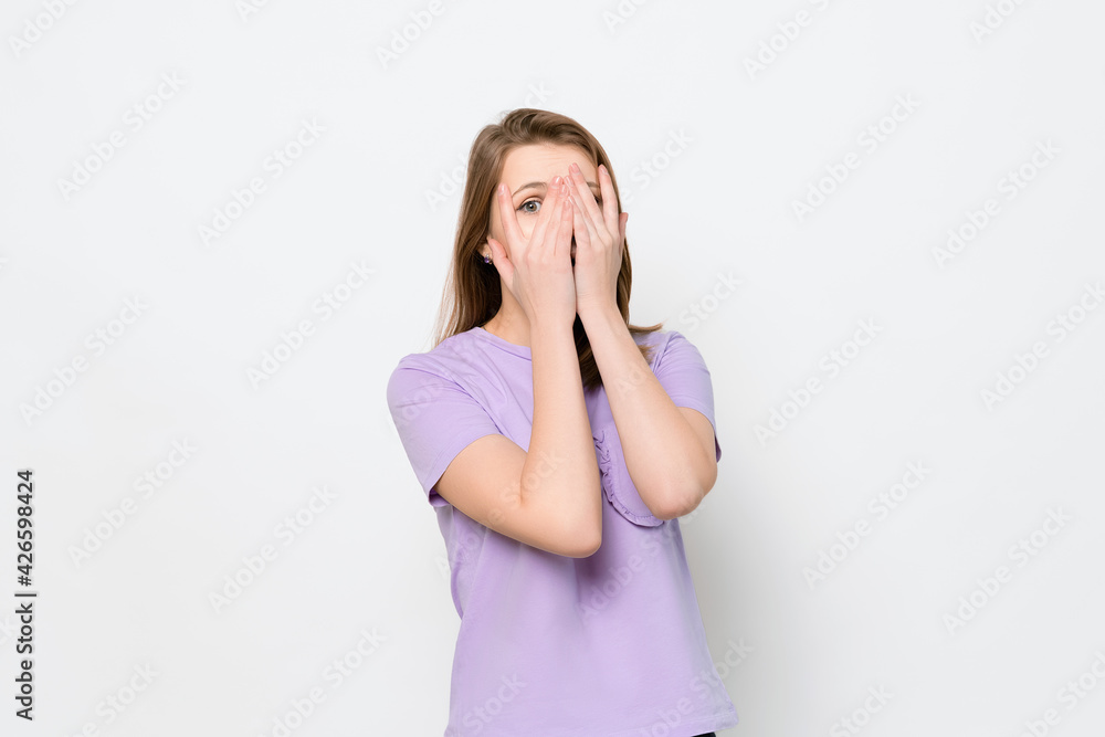 Worried, scared young woman looking between fingers, isolated over white background. Half length portrait Worried, scared young woman looking between fingers, isolated over white background. Half length portrait