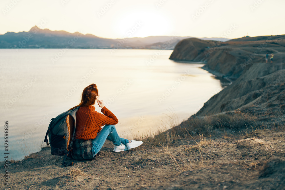 woman hiker with backpack in the mountains at sunset near the sea