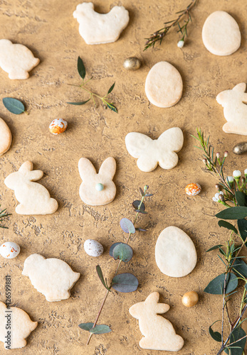 Easter cookies with candies shaped eggs, eucalyptus and flowers, stone background. Butter and sugar cookies. Sweet bakery background. Top view.