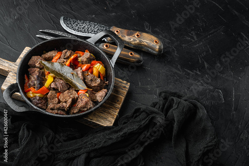 Beef meat and vegetables stew, in cast iron frying pan, on black stone background, with copy space for text