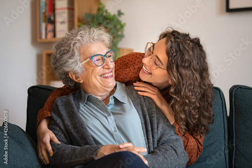 Grandmother and granddaughter laughing and embracing at home photo