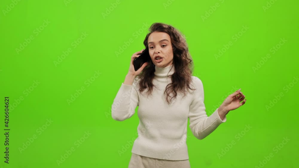 The woman is standing and smiling. She's talking emotionally on the phone. She is waving her hand. She is standing on a green background. Green screen. 4K The woman is standing and smiling. She's talking emotionally on the phone. She is waving her hand. She is standing on a green background. Green screen. 4K