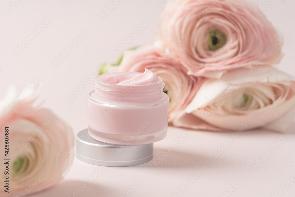 Pink beauty cream in transparent jar on background of delicate flowers. Natural cosmetics for face and body. Close-up and side view on pink background Pink beauty cream in transparent jar on background of delicate flowers. Natural cosmetics for face and body. Close-up and side view on pink background