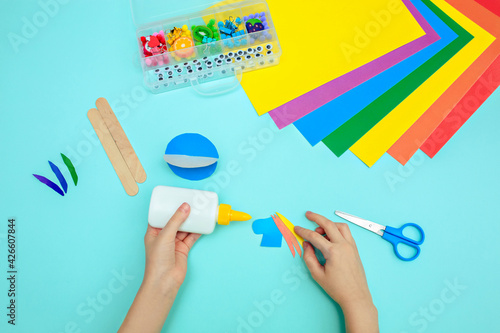 A child glues colored blue paper with glue at the table. Paper crafts for kids.