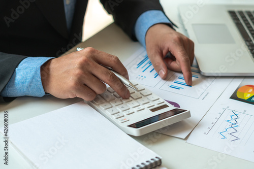 businessman or accountant hand working on calculator to calculate financial data report, accounting document and laptop computer at office, business concept