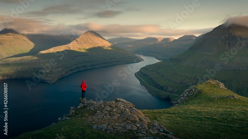 Cuadro en lienzo Man with red jacket at Hvithamar lookout near the town of Gjogv on the Faroe island of Eysturoy with a panoramic view of the fjord and ocean at sunset