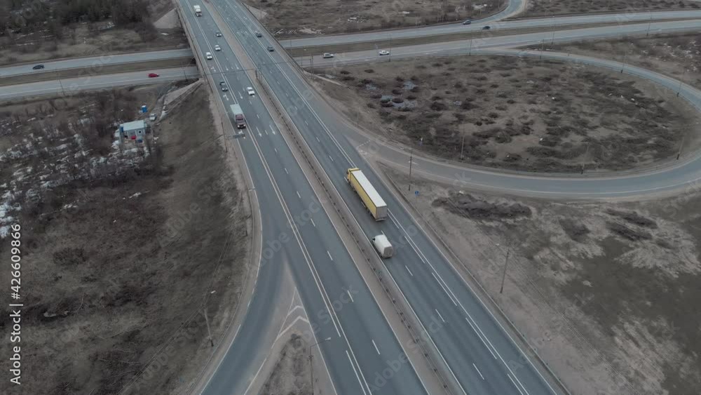 A car interchange with an overpass on a cloudy spring evening in the woods outside the city. Long-distance traffic. Aerial view. The truck passes over the overpass, the camera goes up. A car interchange with an overpass on a cloudy spring evening in the woods outside the city. Long-distance traffic. Aerial view. The truck passes over the overpass, the camera goes up.