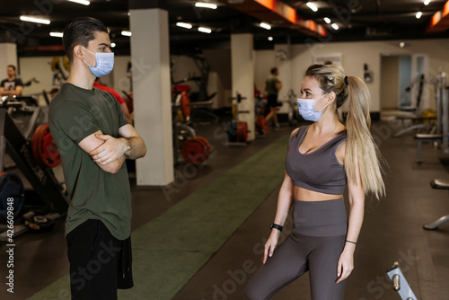 A sports coach and a young woman wearing masks chat in the gym during a pandemic. Sports activities. Coronavirus protection