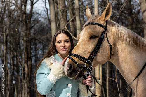 beautiful woman in blue suit with light brown horse in spring forest 